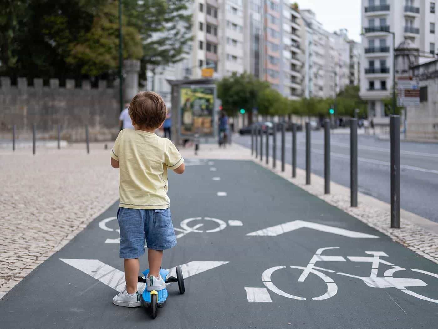 A young child riding a kick scooter along a marked bicycle lane