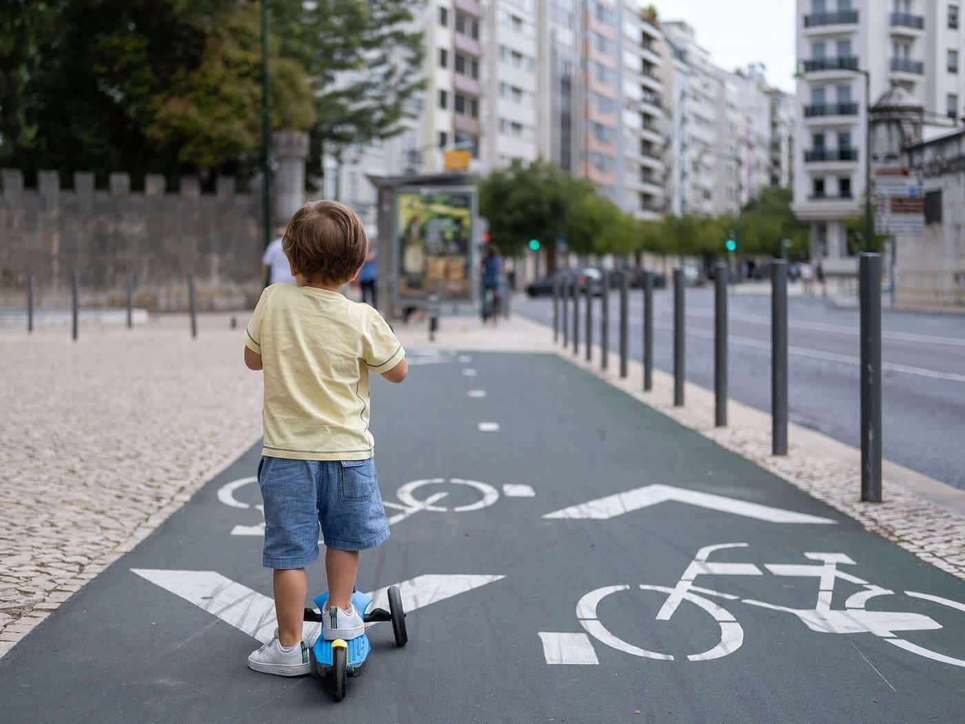 A child riding a kick scooter in a bicycle lane marked on the ground