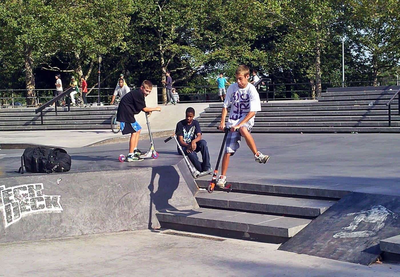 Young people riding scooters and skateboards in a skate park